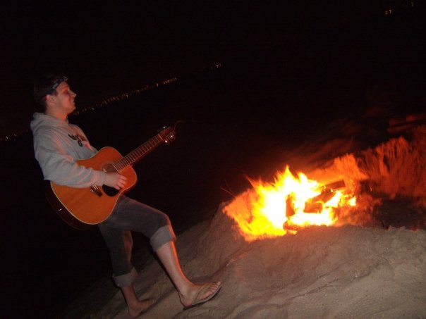 anthony playing guitar at night on the beach with campfire